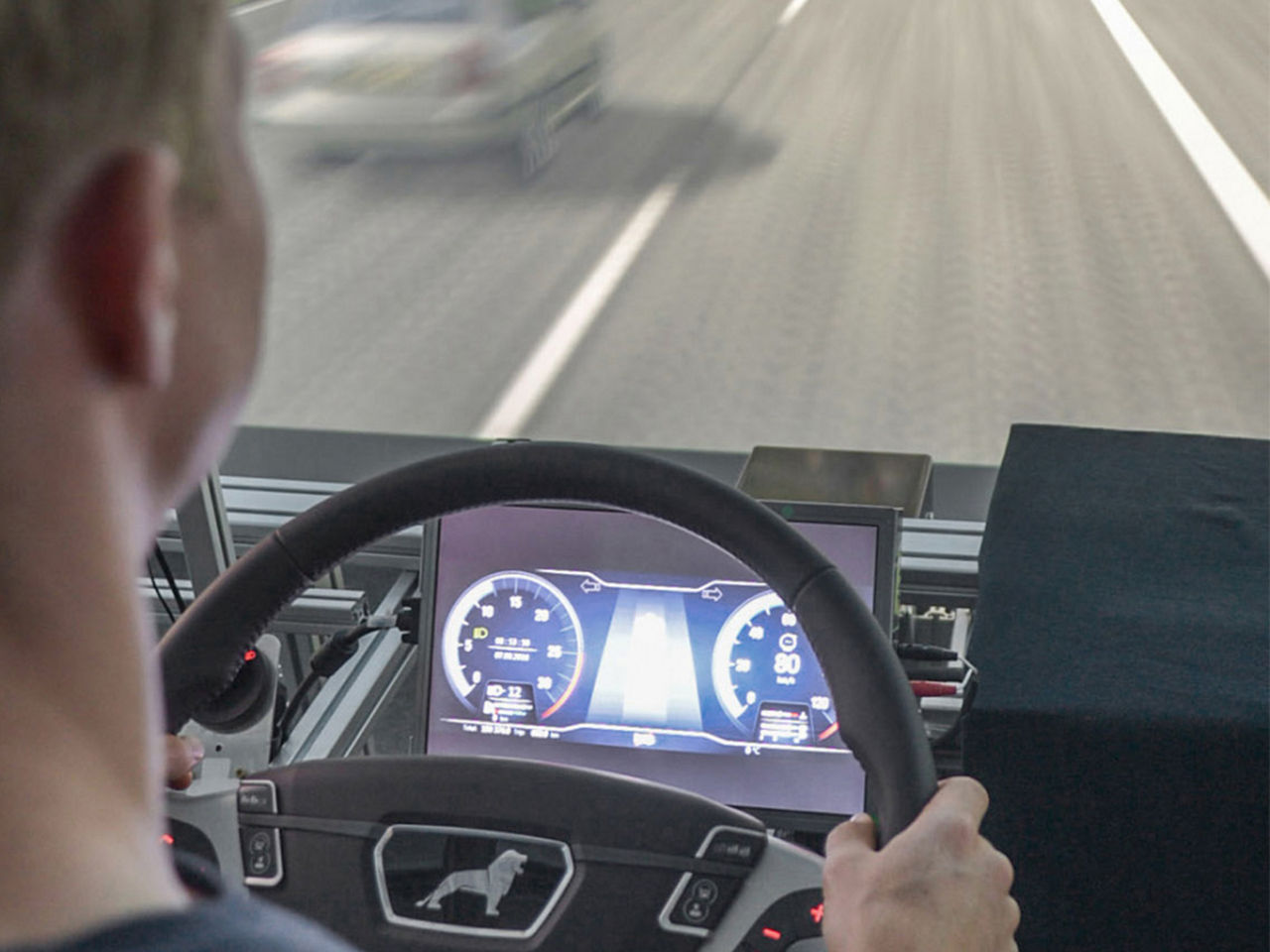 Ein Mann sitzt am Lenkrad eines Simulators und fährt auf einer Straße 