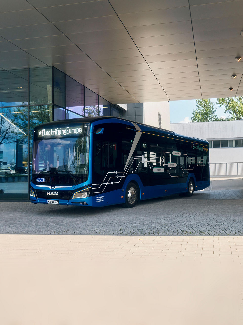 The Lion’s City 12E city bus stands next to a building