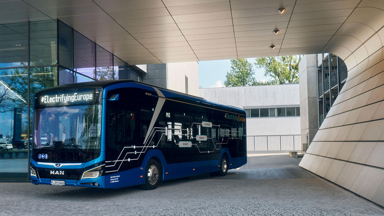 The Lion’s City 12E city bus stands next to a building