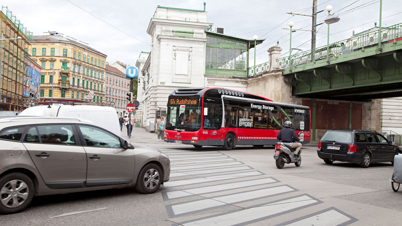 A red MAN Lion’s City hybrid bus crosses a junction