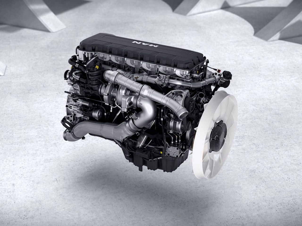 Ein MAN-D30 LKW Motor mit sichtbaren Turboladern, Leitungen und großem Kühlerlüfter, auf grauem Hintergrund.