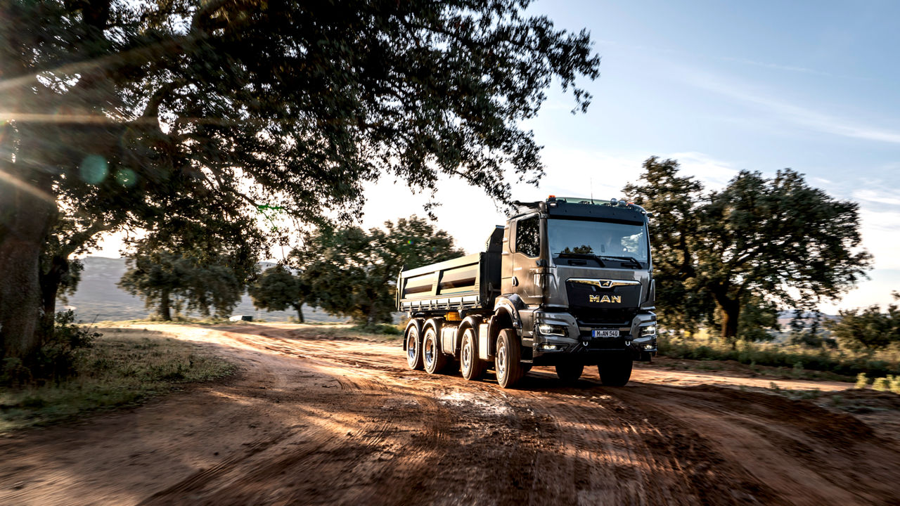 A MAN TGS truck drives along sandy roads in a scenic landscape