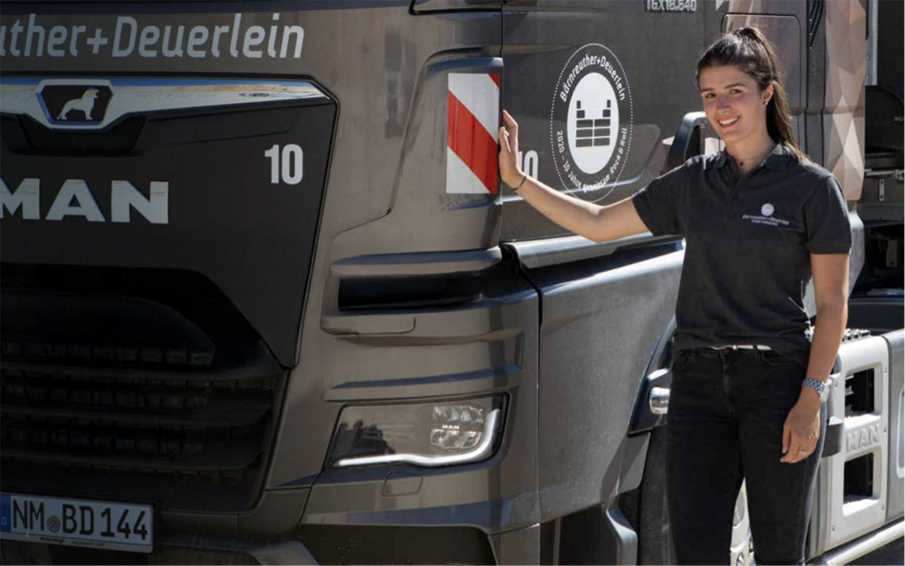 Anna Bärnreuther steht neben einem ihrer Fuhrpark-LKWs und berührt die Fahrertür eines MAN Trucks