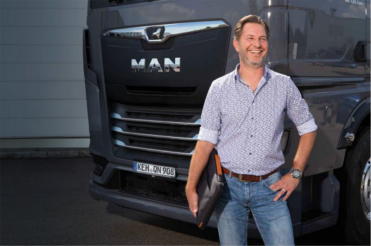 Jochen Wild, Prokurist der Ralf Steller Spedition GmbH, steht mit einer Mappe vor einem schwarzen MAN Truck.