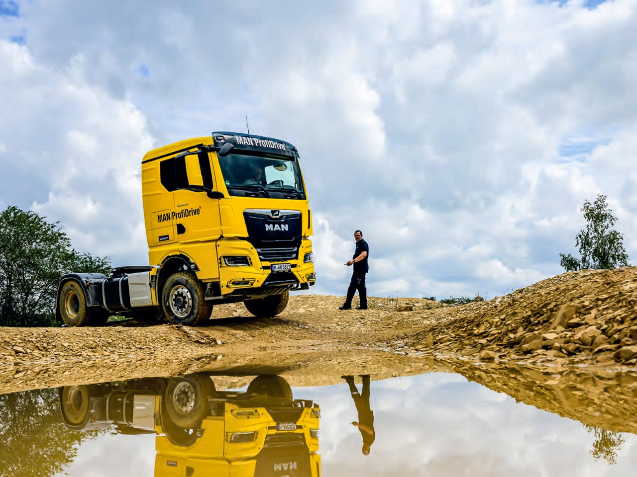 Gelber MAN TGX steht auf sandigem Gelände, eine Person nähert sich bei bewölktem Himmel.