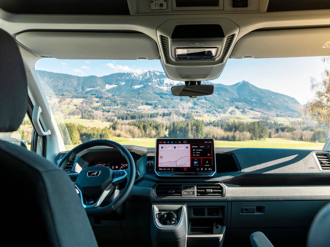 MAN TGE Cockpit mit Multifunktionslederrad, digitalem Kombiinstrument und Blick auf eine Berglandschaft.