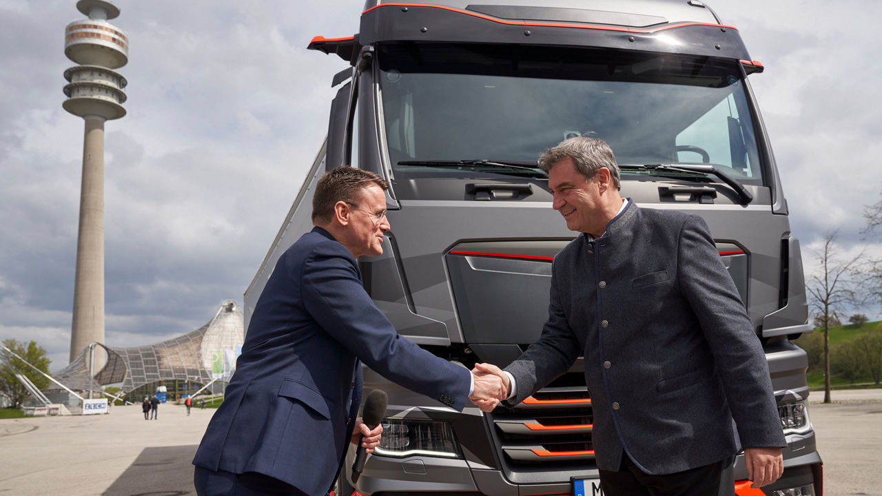 Dr Markus Söder and Alexander Vlaskamp shake hands. They are standing in front of a MAN truck on the Olympic grounds in Munich. 