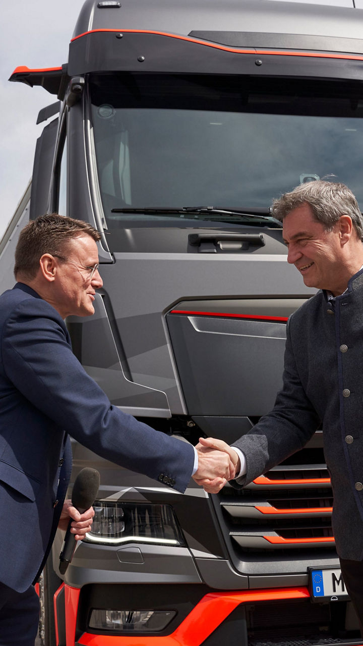 Dr Markus Söder and Alexander Vlaskamp shake hands. They are standing in front of a MAN truck on the Olympic grounds in Munich. 
