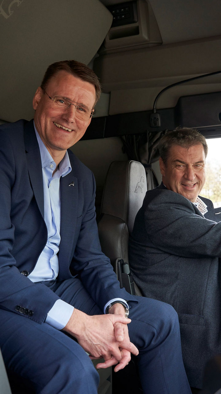 Closeup of dr Markus Söder and Alexander Vlaskamp in the cockpit of a truck. Both laugh at the camera. 