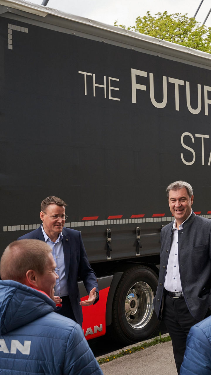 Dr Markus Söder and Alexander Vlaskamp are standing in front of a truck with three other men. 