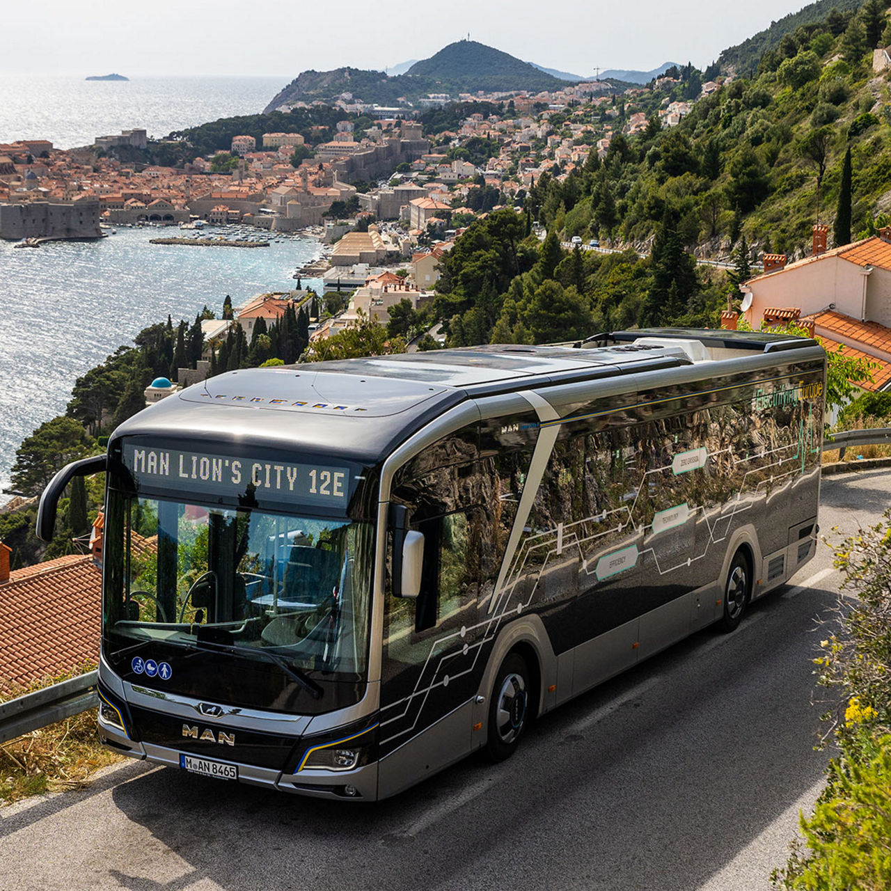 A MAN Lion’s City E driving along a road by the sea.