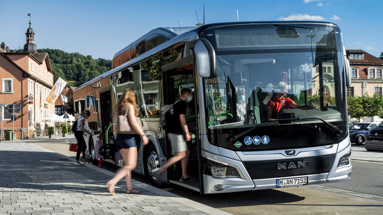 A parked MAN bus at a bus stop. The doors are open and people get in. . 