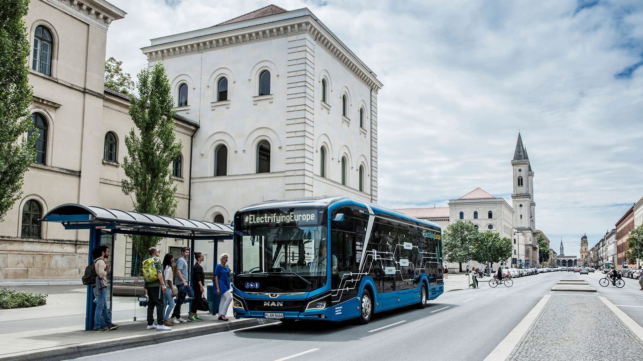A MAN bus is at a bus stop in Munich. People stand in line ready to board. 