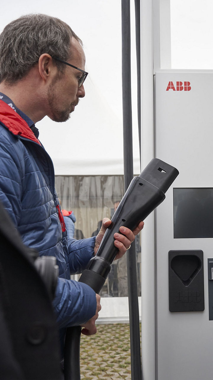 Ein Mann hält den Stecker von einer Ladesäule in der Hand
