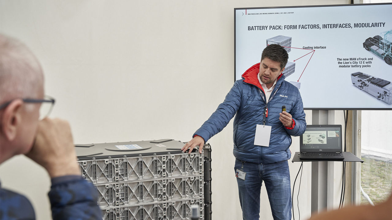 Dr. Markus Pröpster zeigt auf einen Battery Pack vor einem Bildschirm