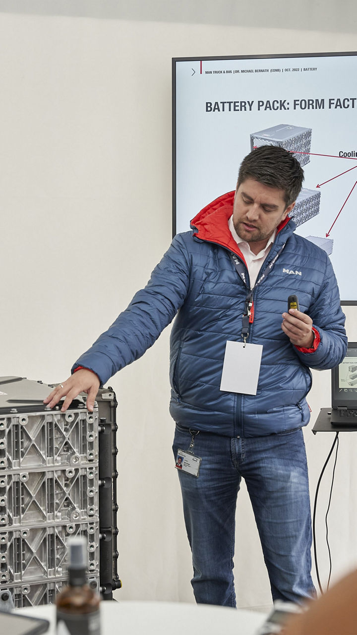 Dr. Markus Pröpster zeigt auf einen Battery Pack vor einem Bildschirm