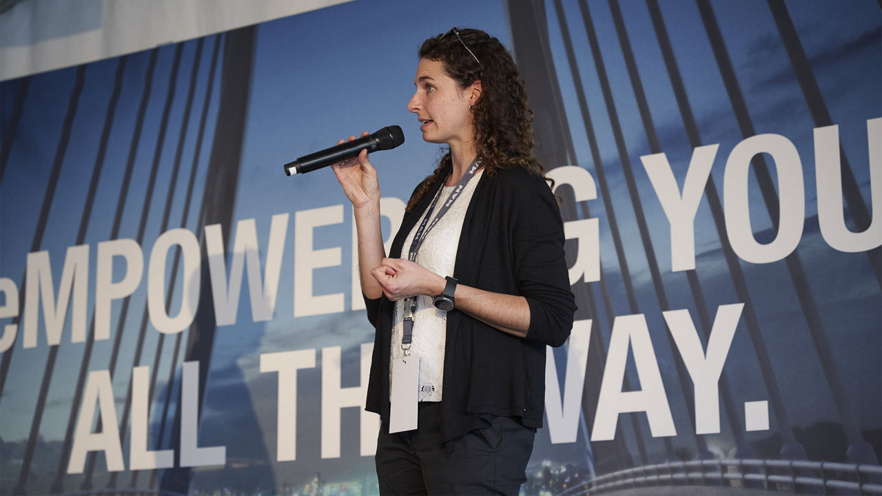 MAN eMobility-Expertin Raphaela Natterer spricht vor einer Leinwand in ein Mikrofon