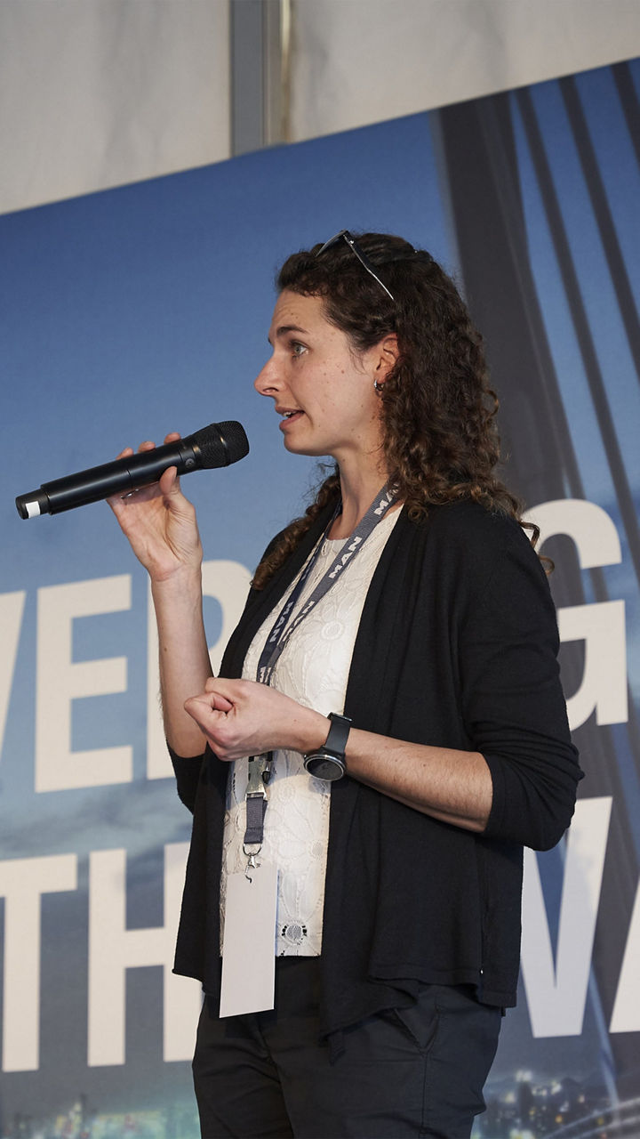 MAN eMobility-Expertin Raphaela Natterer spricht vor einer Leinwand in ein Mikrofon