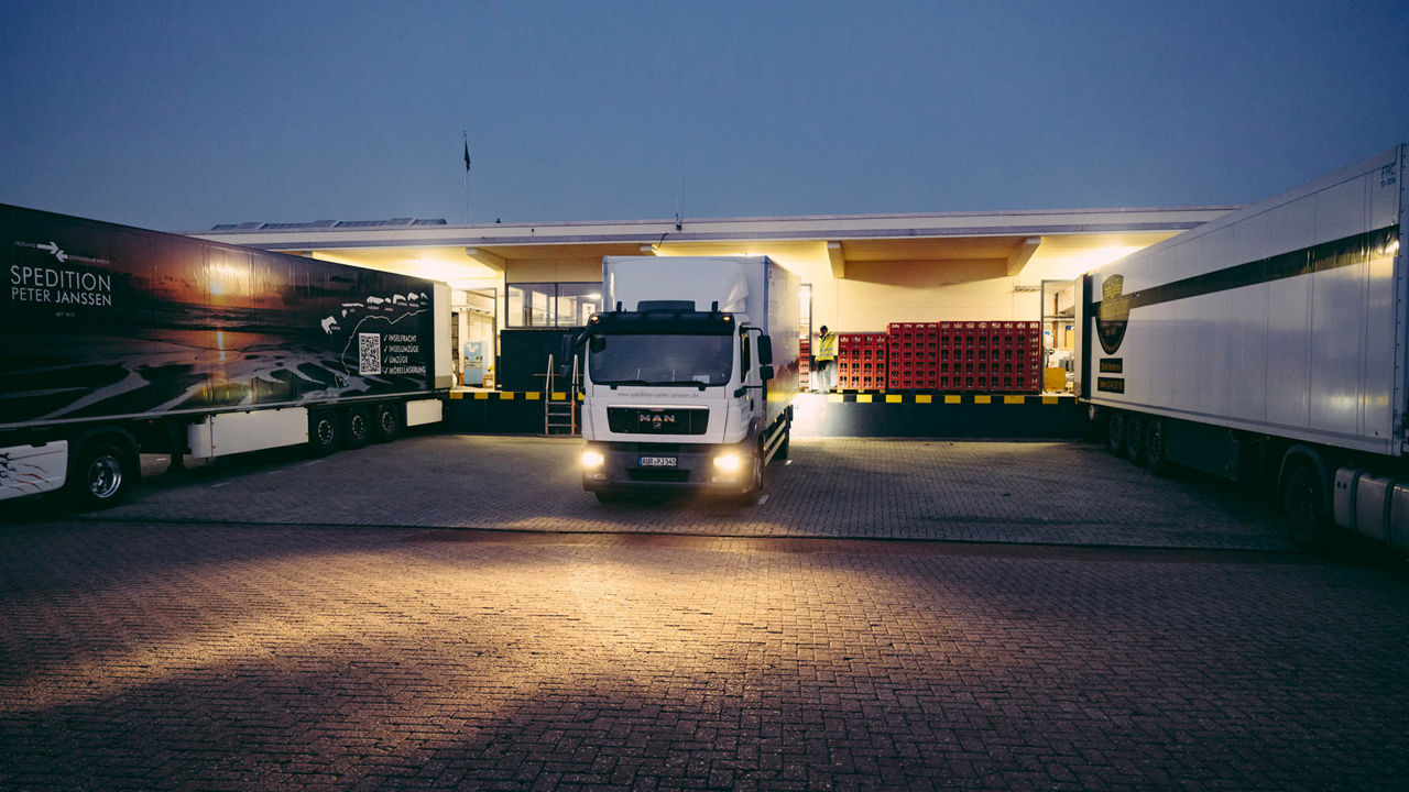 Speditionsfahrzeuge parken vor einer Halle. Eines fährt los. 