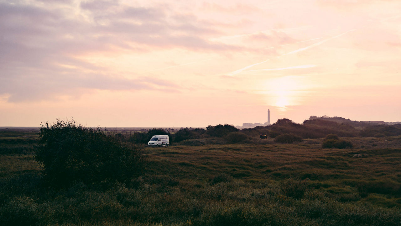 Ein MAN Transporter fährt durch eine Landschaft. Ein Abendhimmel erstreckt sich im Hintergrund. 