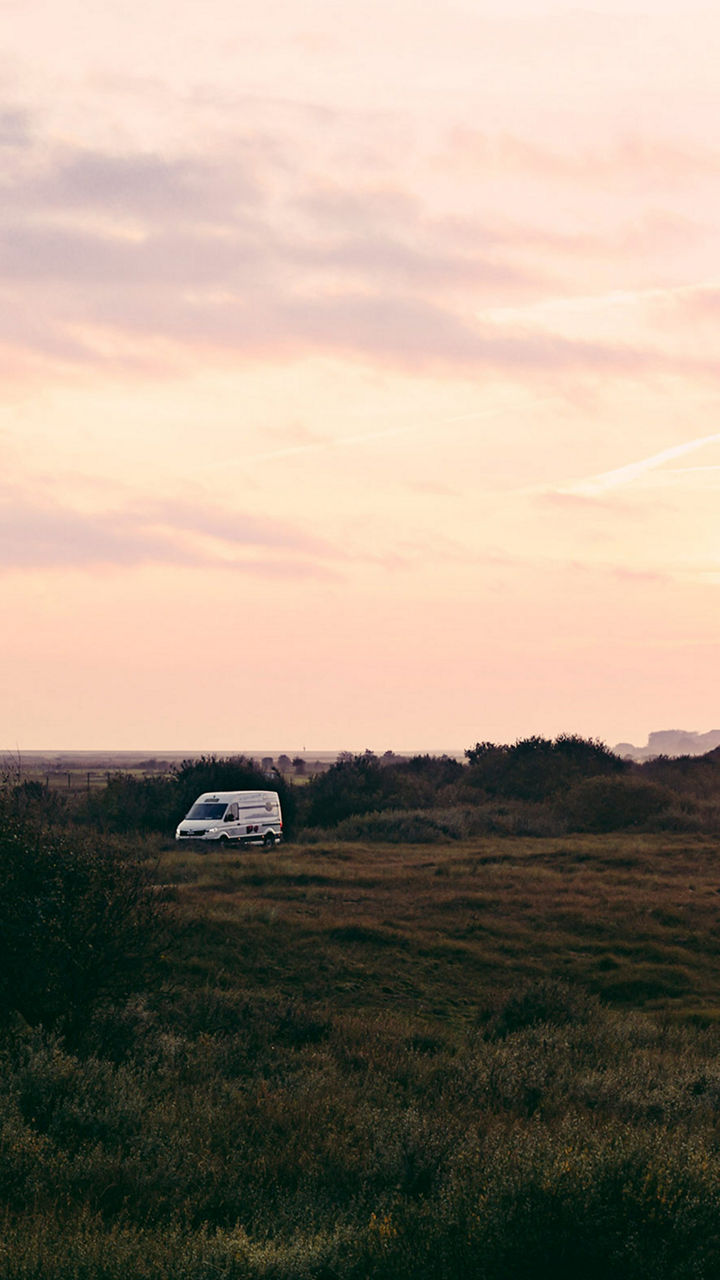 Ein MAN Transporter fährt durch eine Landschaft. Ein Abendhimmel erstreckt sich im Hintergrund. 