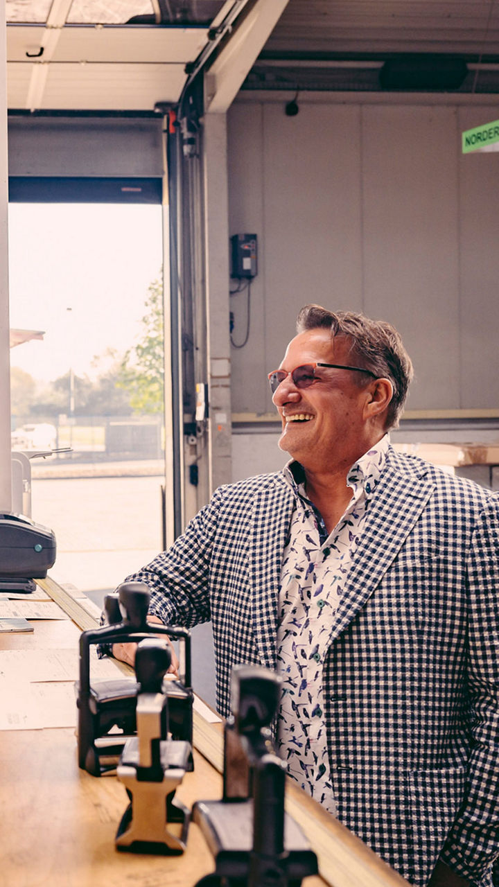 Spediteur Fischer steht an einem Tresen und unterhält sich mit einem Mann in Arbeitskleidung. 