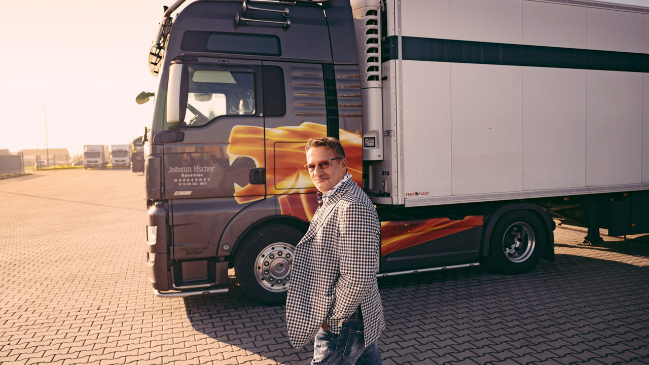 Spediteur Fischer läuft über einen Platz. Im Hintergrund parkt ein Speditionstruck. 