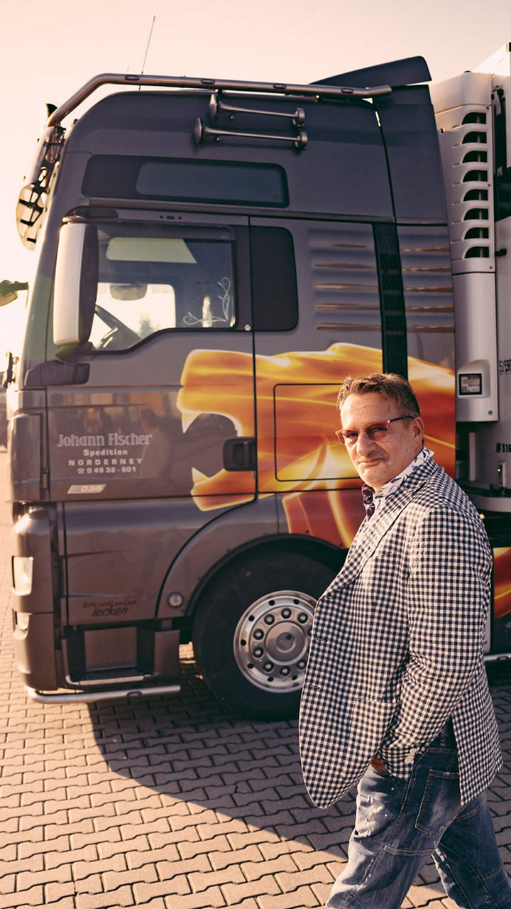 Spediteur Fischer läuft über einen Platz. Im Hintergrund parkt ein Speditionstruck. 