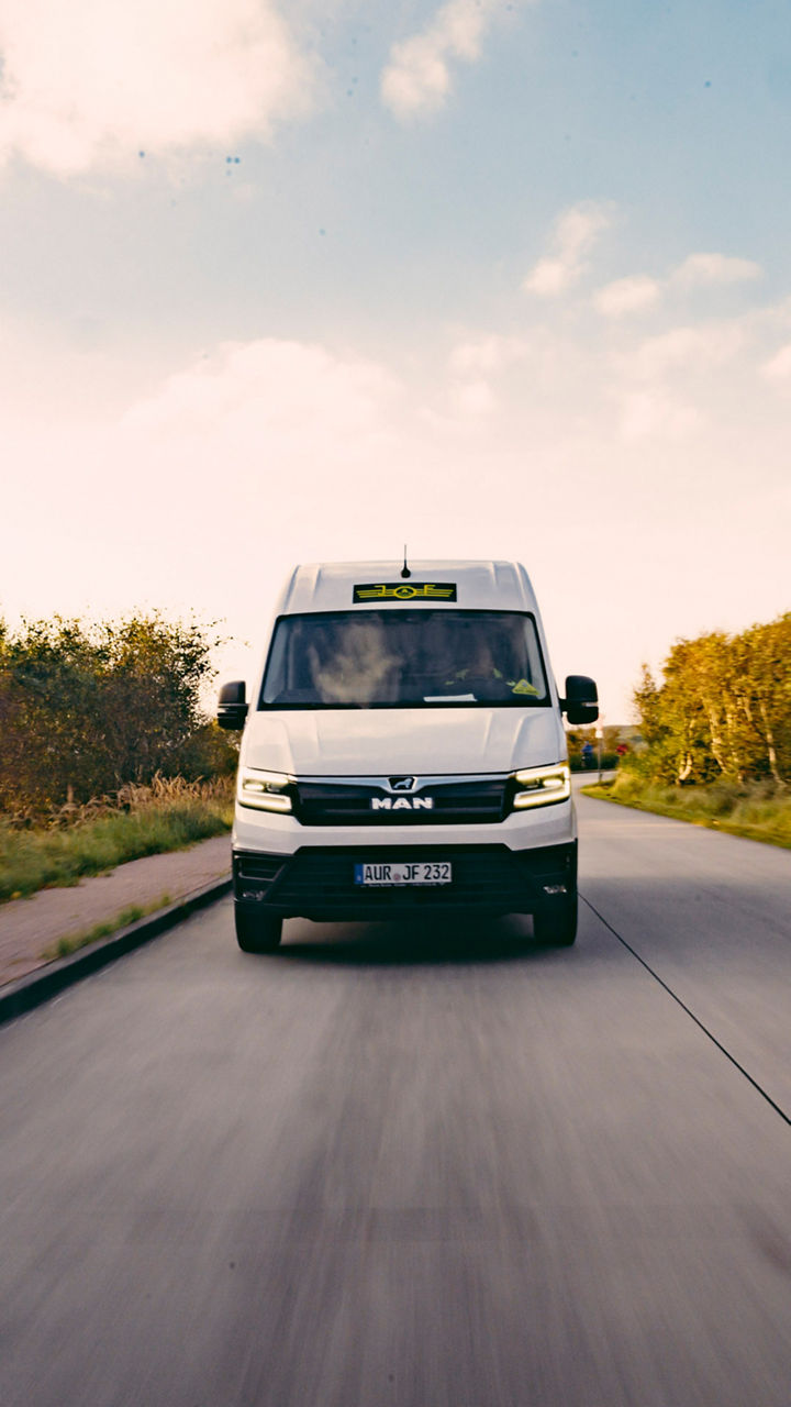 Ein MAN Transporter fährt auf einer Straße durch eine Landschaft. 