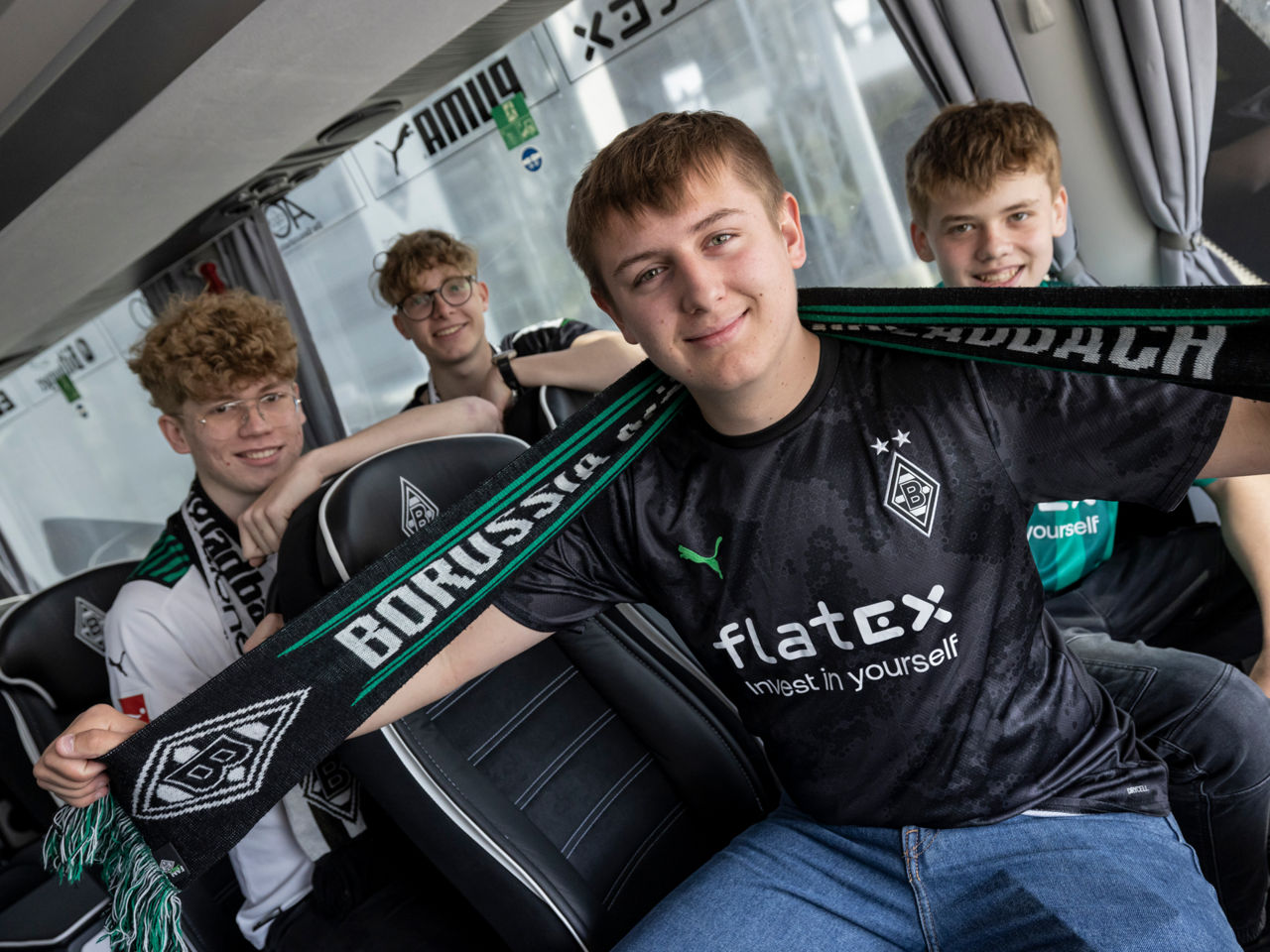 Vier Jungs sitzen in einem Reisebus, gekleidet in Fan-Kleidung von Borussia Mönchengladbach