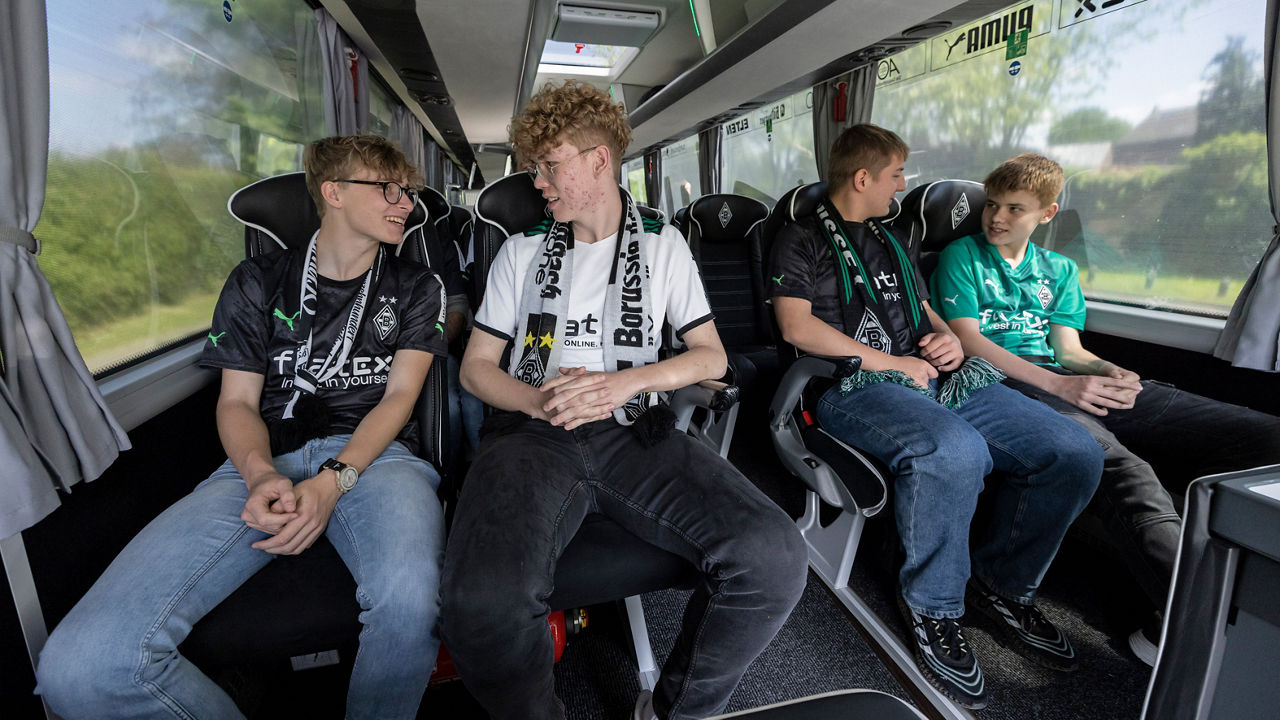 Vier Jungs sitzen in einem Reisebus, gekleidet in Fan-Kleidung von Borussia Mönchengladbach