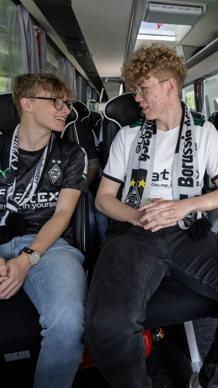 Vier Jungs sitzen in einem Reisebus, gekleidet in Fan-Kleidung von Borussia Mönchengladbach