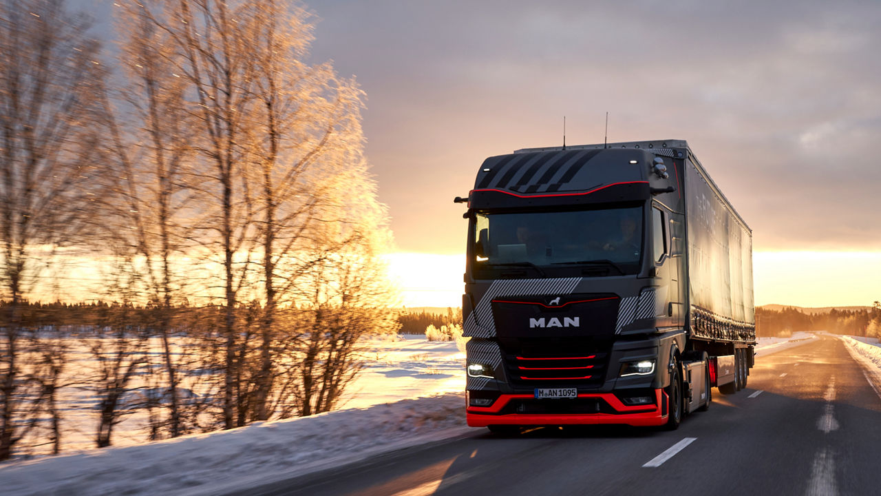 A MAN truck drives on a road through a snow-covered landscape. Evening sky in the background 