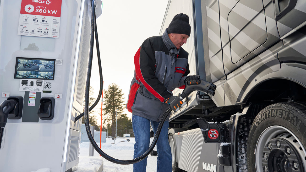 A man stands at a gas station and fills up a truck. 