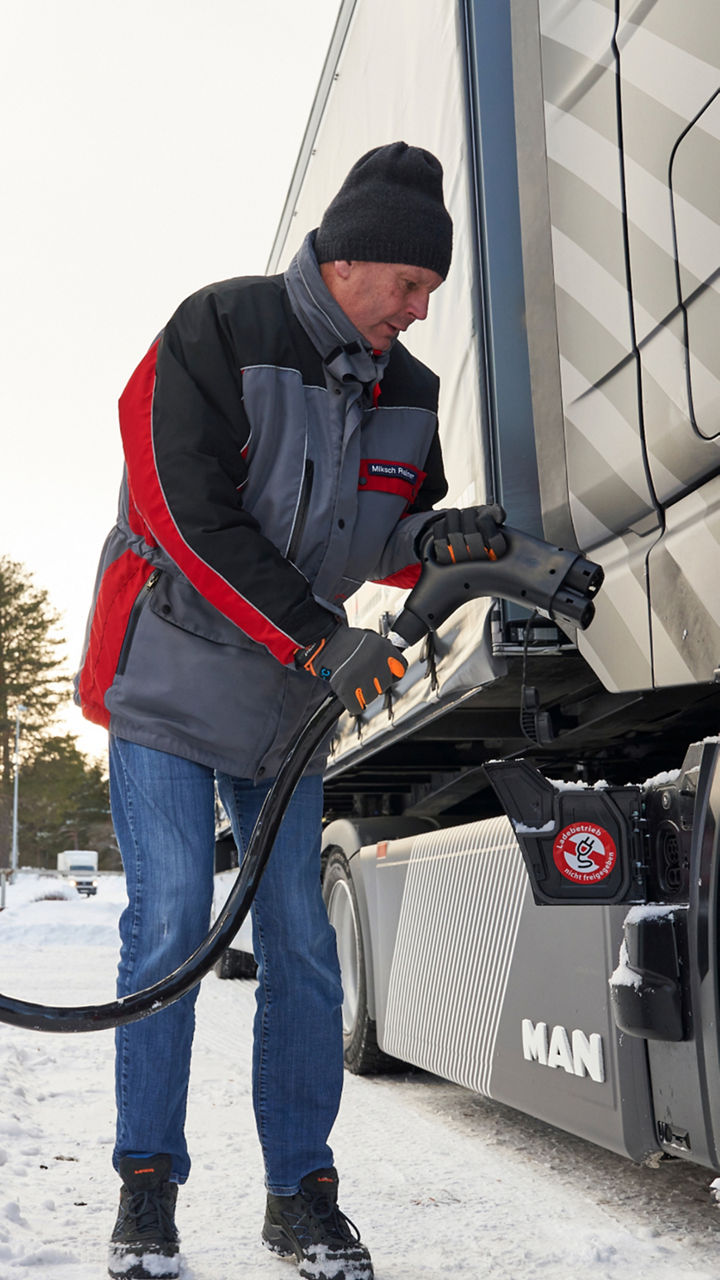 A man stands at a gas station and fills up a truck. 