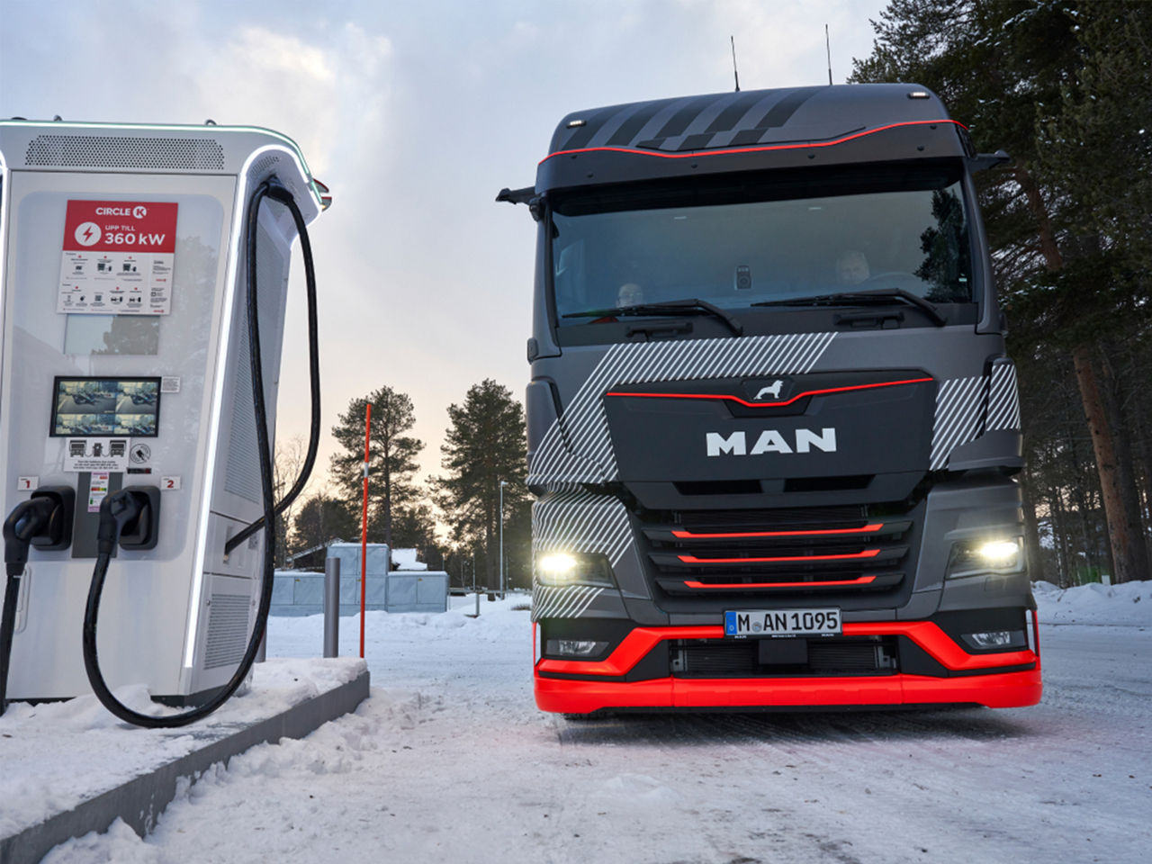A MAN truck is parked on a snow-covered road at a gas station. 