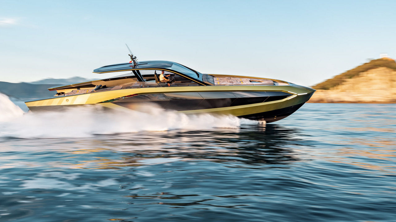 Eine Yacht gleitet durchs Wasser. Im Hintergrund felsiges und bewachsenes Festland. 