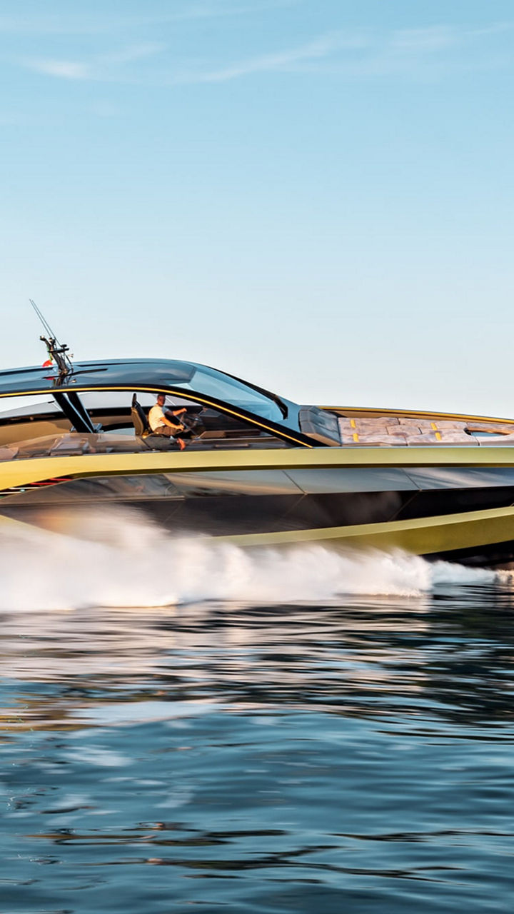 Eine Yacht gleitet durchs Wasser. Im Hintergrund felsiges und bewachsenes Festland. 