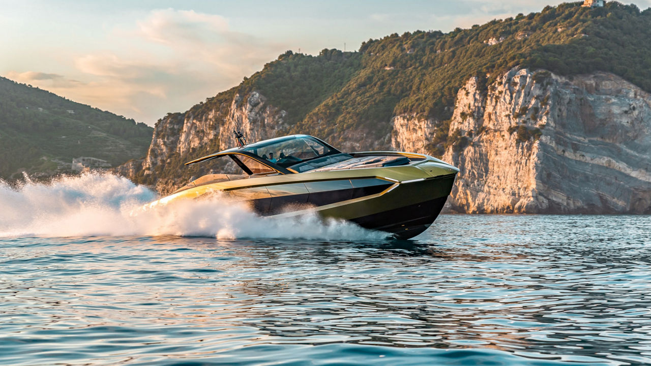 Eine Yacht gleitet durchs Wasser. Im Hintergrund felsiges und bewachsenes Festland. 