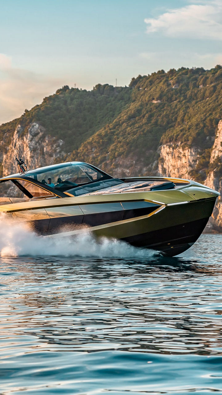 Eine Yacht gleitet durchs Wasser. Im Hintergrund felsiges und bewachsenes Festland. 