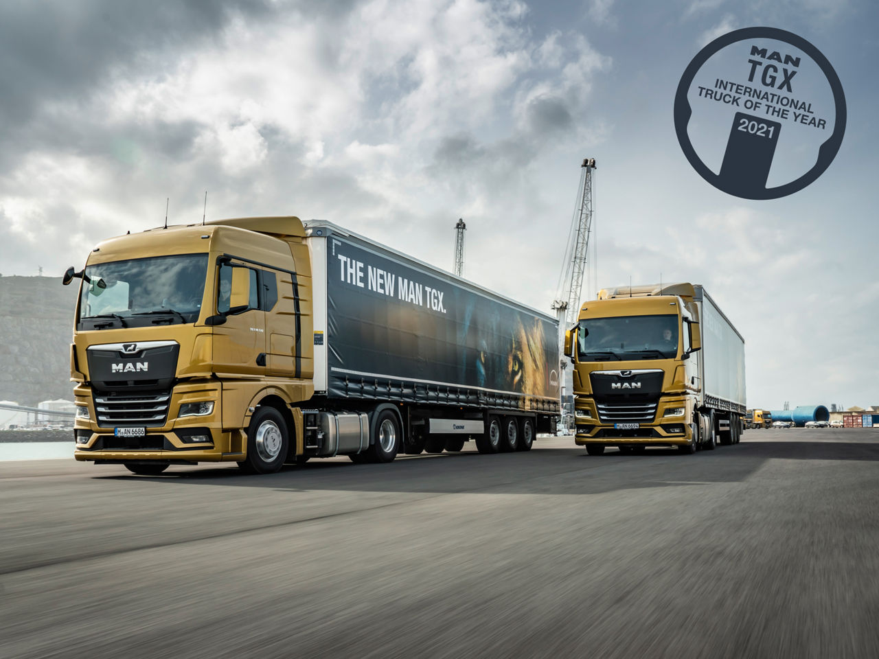 Zwei MAN TGX fahren am Ufer eines Flusses in einem Industriegebiet entlang.