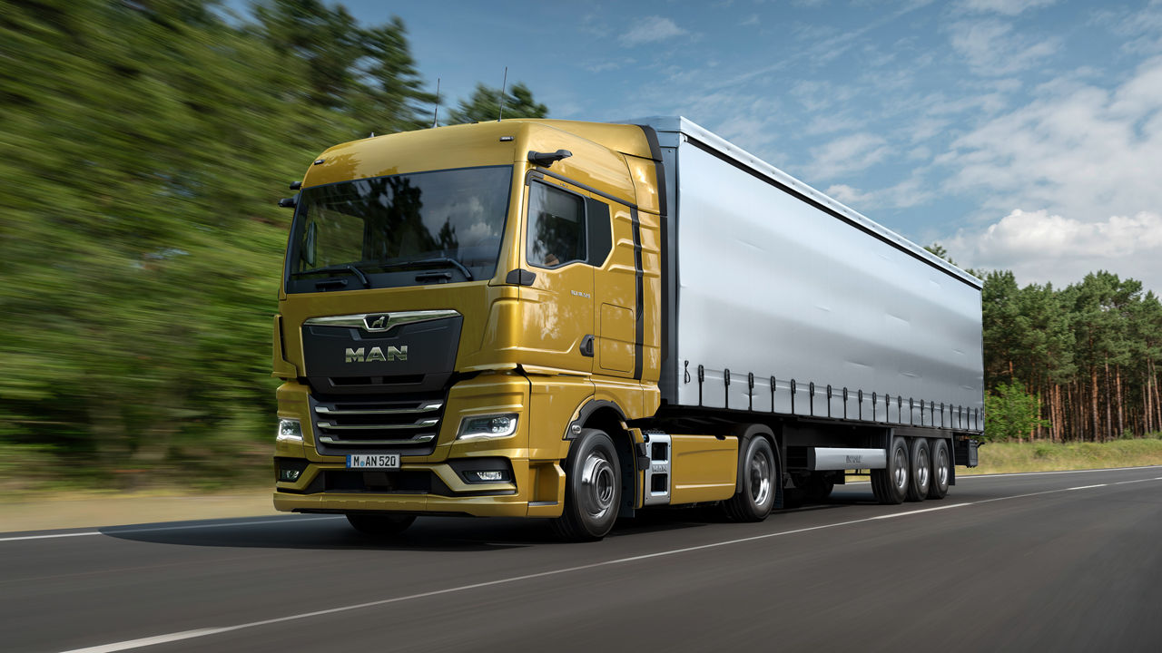 MAN TGX їде по діагоналі спереду по сільській дорозі біля лісу.