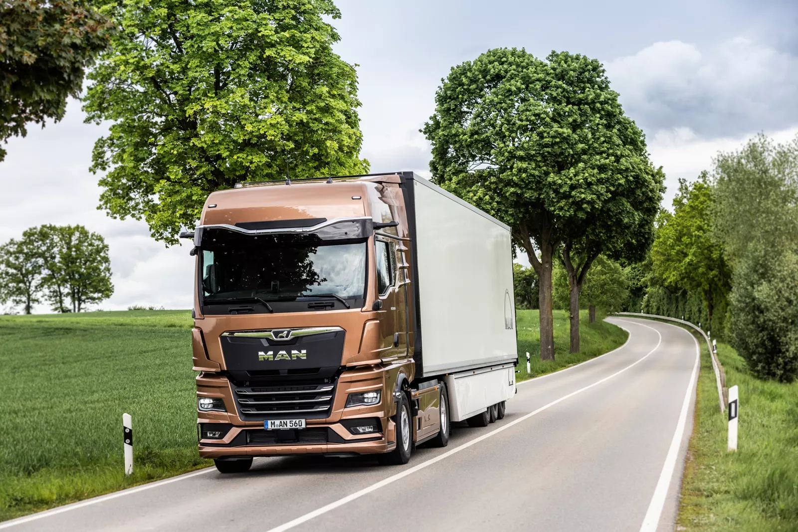 Der MAN TGX schräg von vorne fahrend auf einer Landstraße an einem Wald.