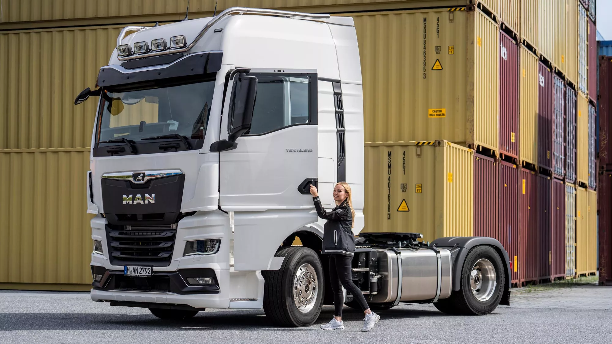 MAN Lkw vor gestapelten Containern im Containerhafen, Frau öffnet die Fahrertür des weißen Lkws