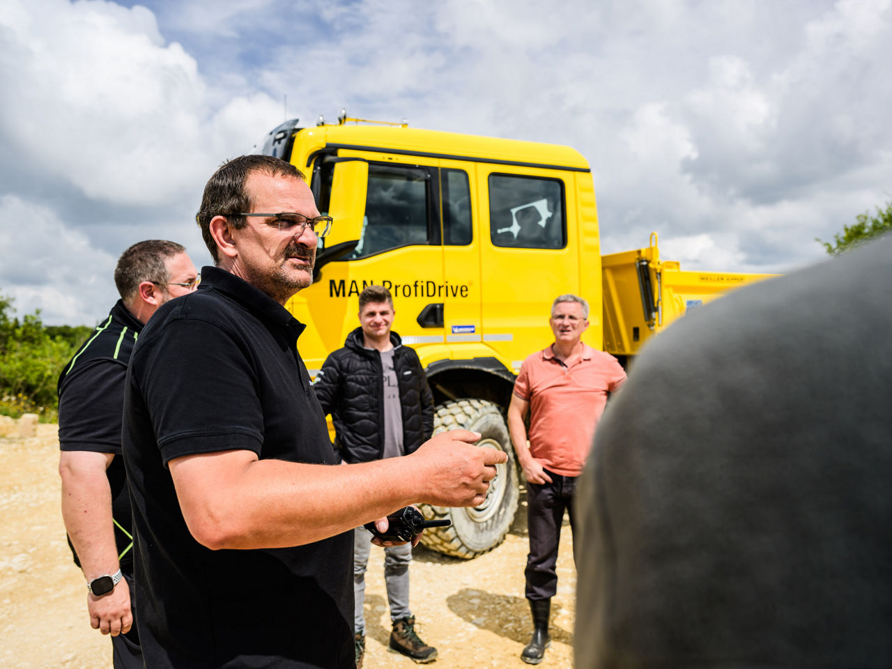 Bei einem MAN ProfiDrive Training stehen mehrere Personen vor einem gelben MAN Truck auf unbefestigtem Gelände. Der Lkw ist für Offroad-Einsätze ausgelegt.