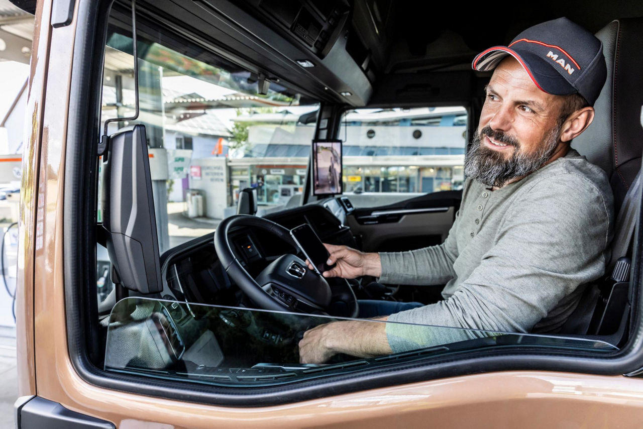 Lkw-Fahrer sitzt entspannt im Führerhaus eines Trucks und schaut lächelnd nach draußen.