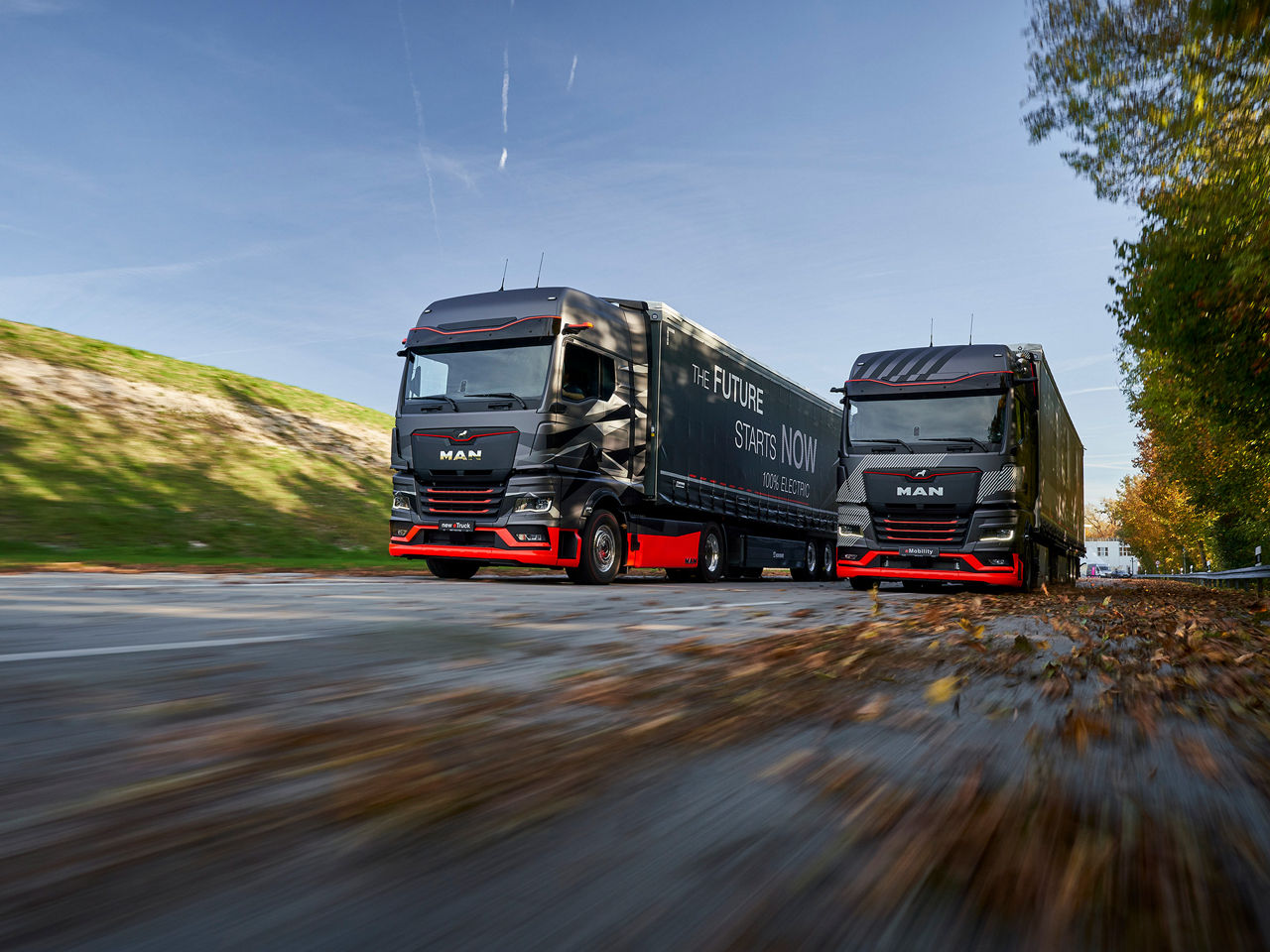Two MAN eTrucks driving on autumn road, side by side