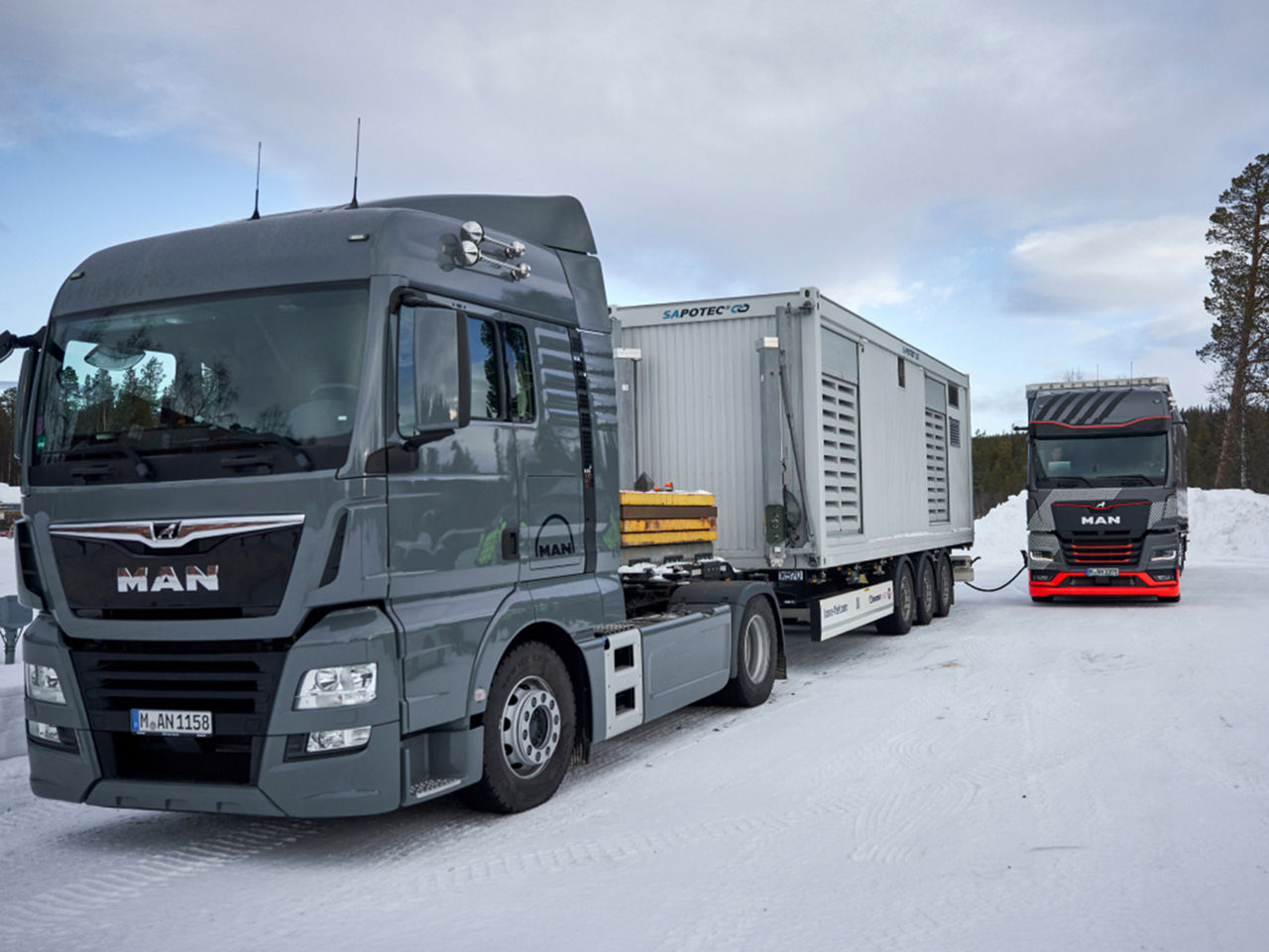 Two MAN trucks are parked on a snow-covered area. 